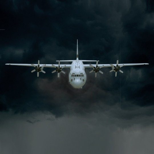 Front view of a C-130J aircraft flying through dark clouds
