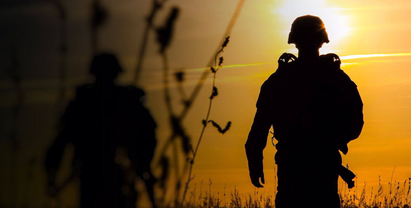 Silhouettes of the back of two soldiers in a field at dusk