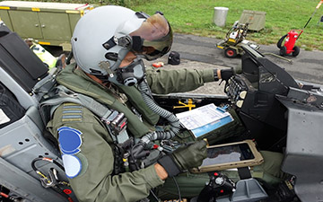 Fighter pilot sitting in a grounded jet looking at a tablet
