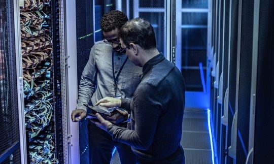 2 men in a server room discussing cybersecurity for government and looking at a tablet